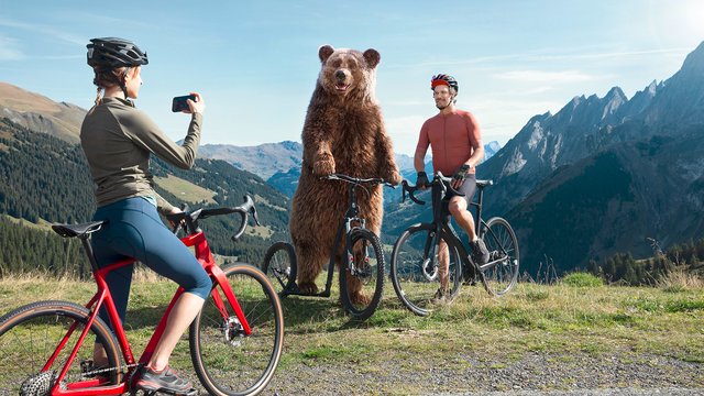 Ein Bär posiert für ein Foto mit zwei Radfahrer:innen